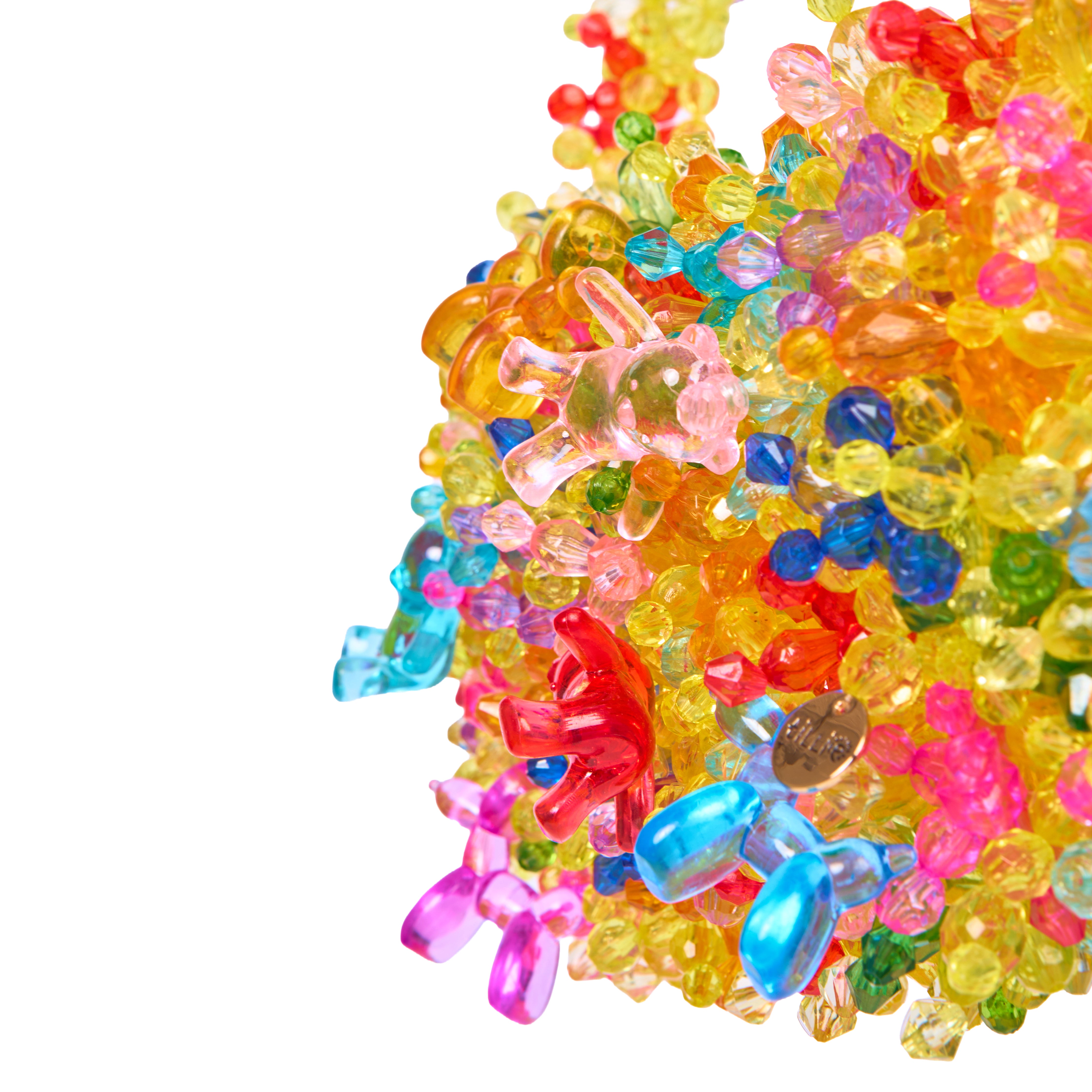 A pile of colorful translucent plastic toy beads and small gummy-shaped pieces in bright yellow, pink, blue, red, orange, and green on a white background.